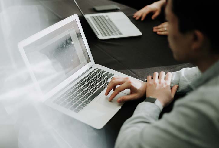 Person working on a laptop with colleagues around a meeting table.
