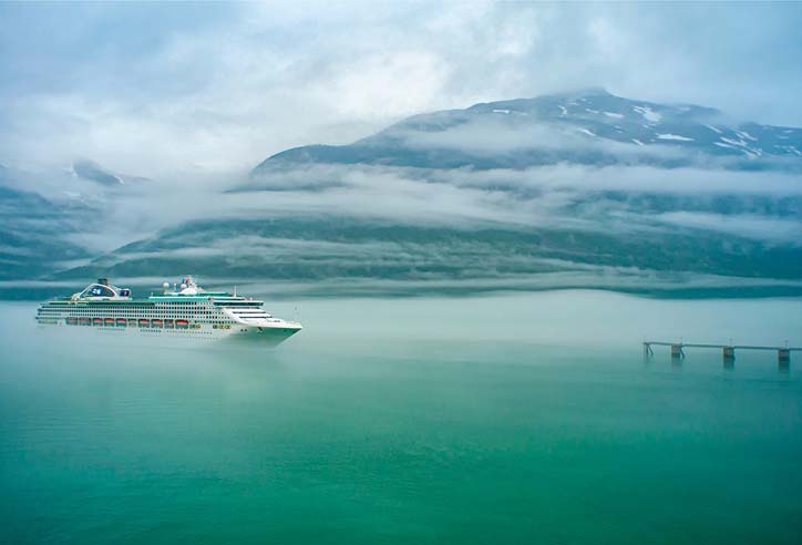 Cruise ship sailing on calm turquoise water in front of mist-covered mountains.