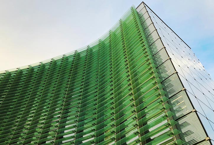 Modern building with a curved green glass facade and horizontal louvres viewed from below.
